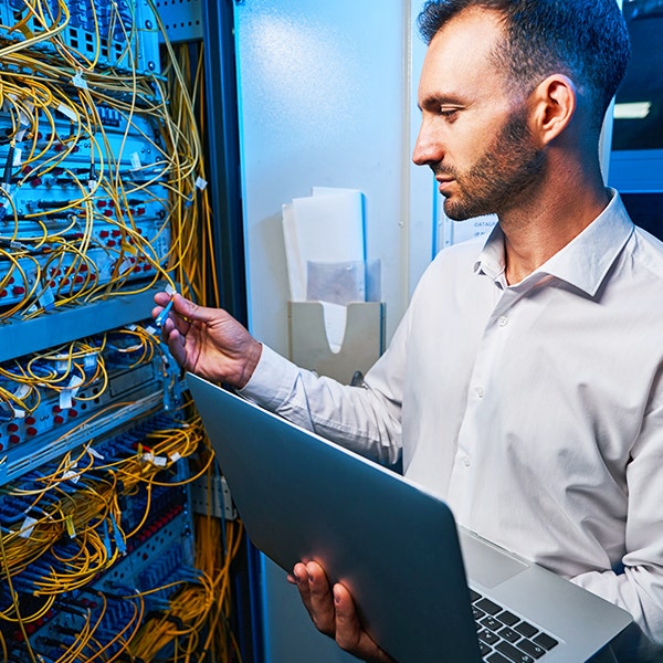 A man holding a laptop inspecting yellow fiberoptic cables