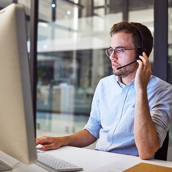 A male associate talking into his headset while he uses his desktop