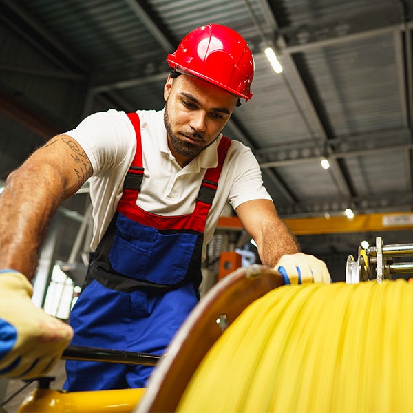 Male associate dressed in blue overalls and a red hardhat pushing a wire reel holder