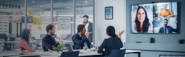 Three people in a conference room waving hi during a virtual meeting