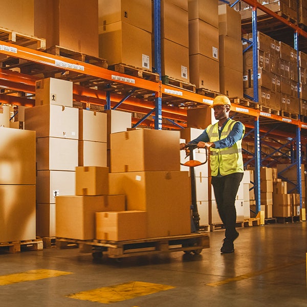 A man pushing a trolley full of boxes through a warehouse