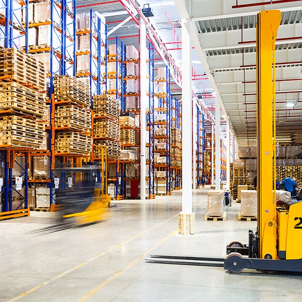 Forklifts driving through a warehouse filled with pallets
