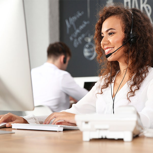 A woman with curly brown hair, a white shirt, and wearing a headset while working at a desktop