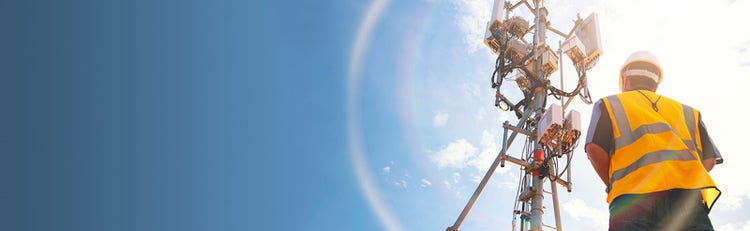 Lineman wearing a white hardhat and orange vest looking up at a telephone pole