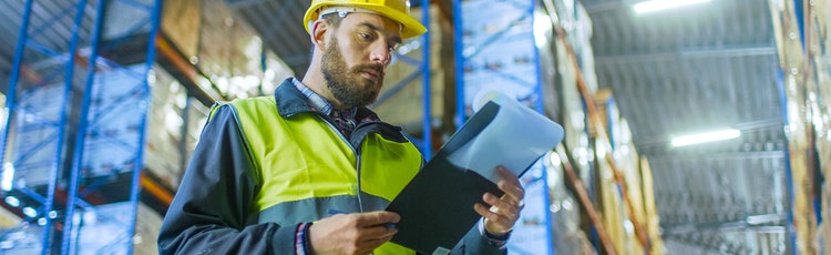 Male associate looking at a clipboard in a warehouse while in uniform