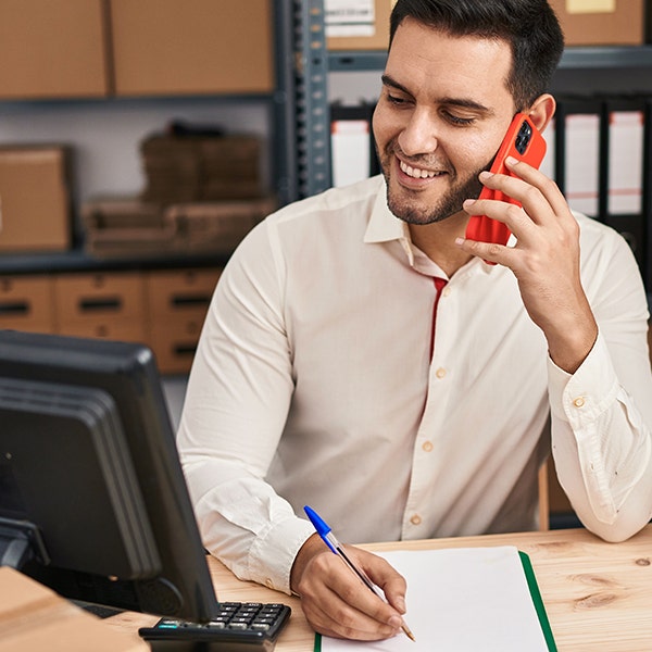 Male associate sitting at his desk on his red iPhone and taking notes